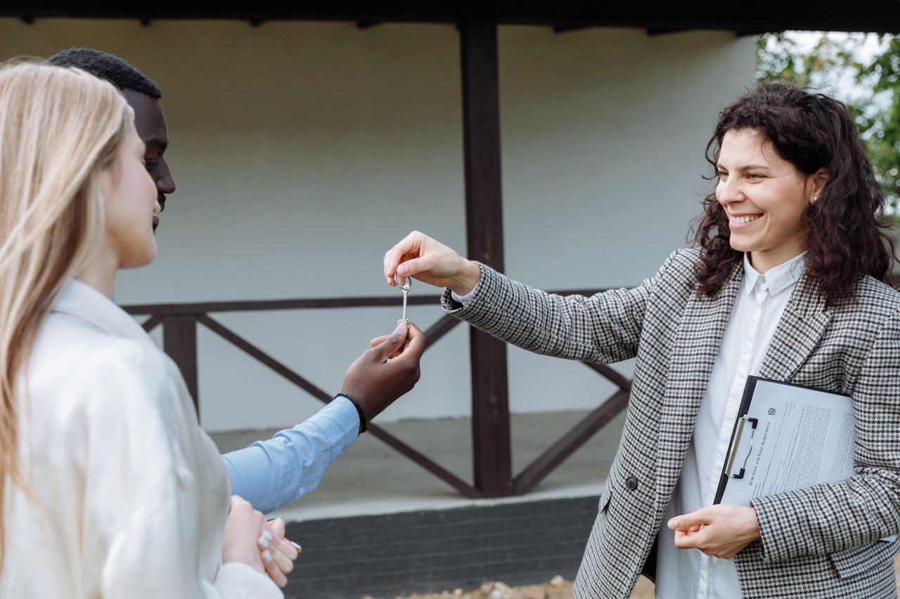 Offerings Real estate agent giving house keys to a happy couple outside their new home.