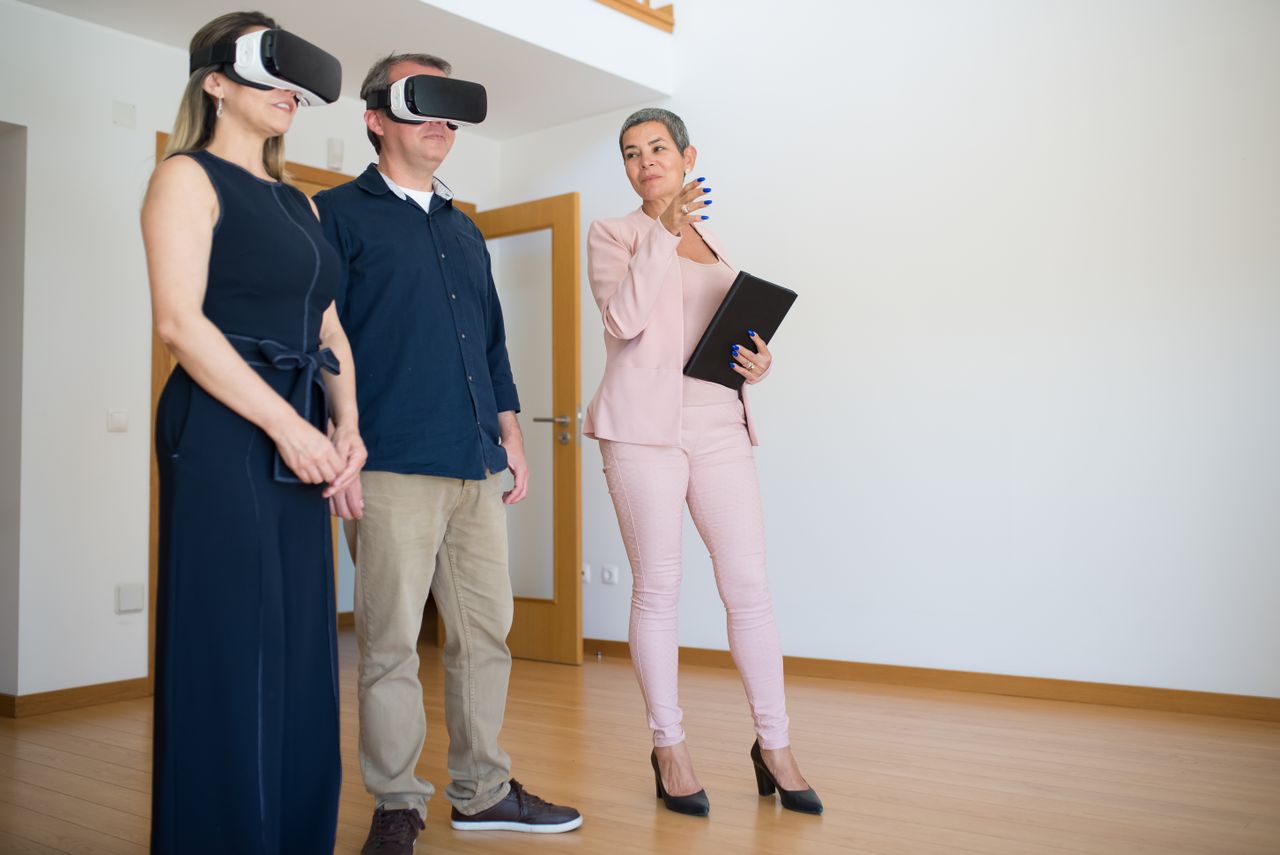 Home A couple uses virtual reality headsets for a house tour guided by a real estate agent indoors.