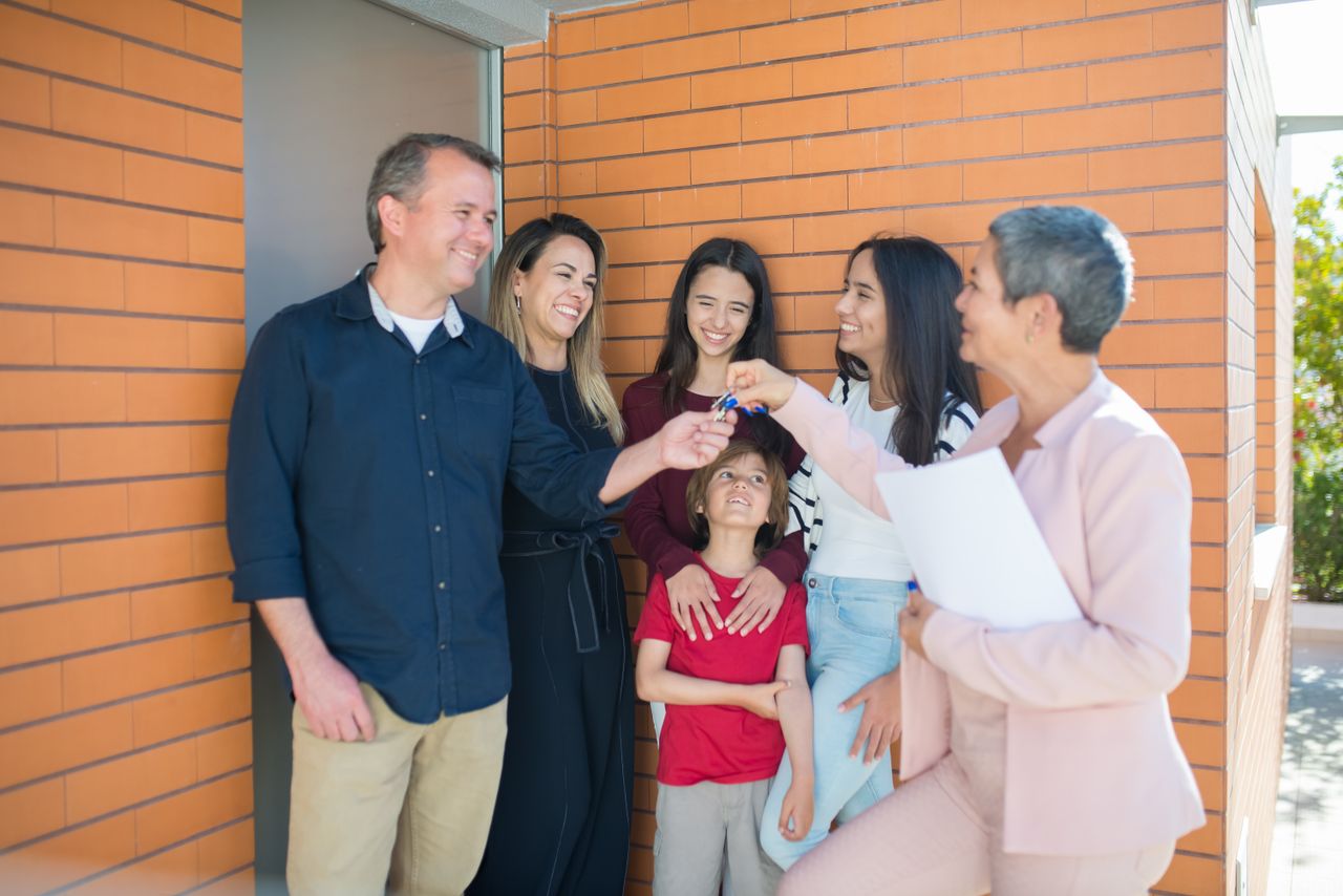 Offerings Family joyfully receiving keys to their new home outdoors, symbolizing real estate success.
